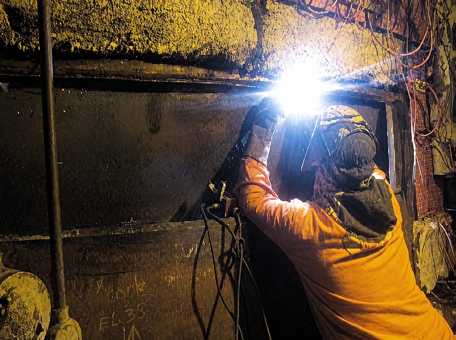Worker in orange safety gear welding on a metal surface.